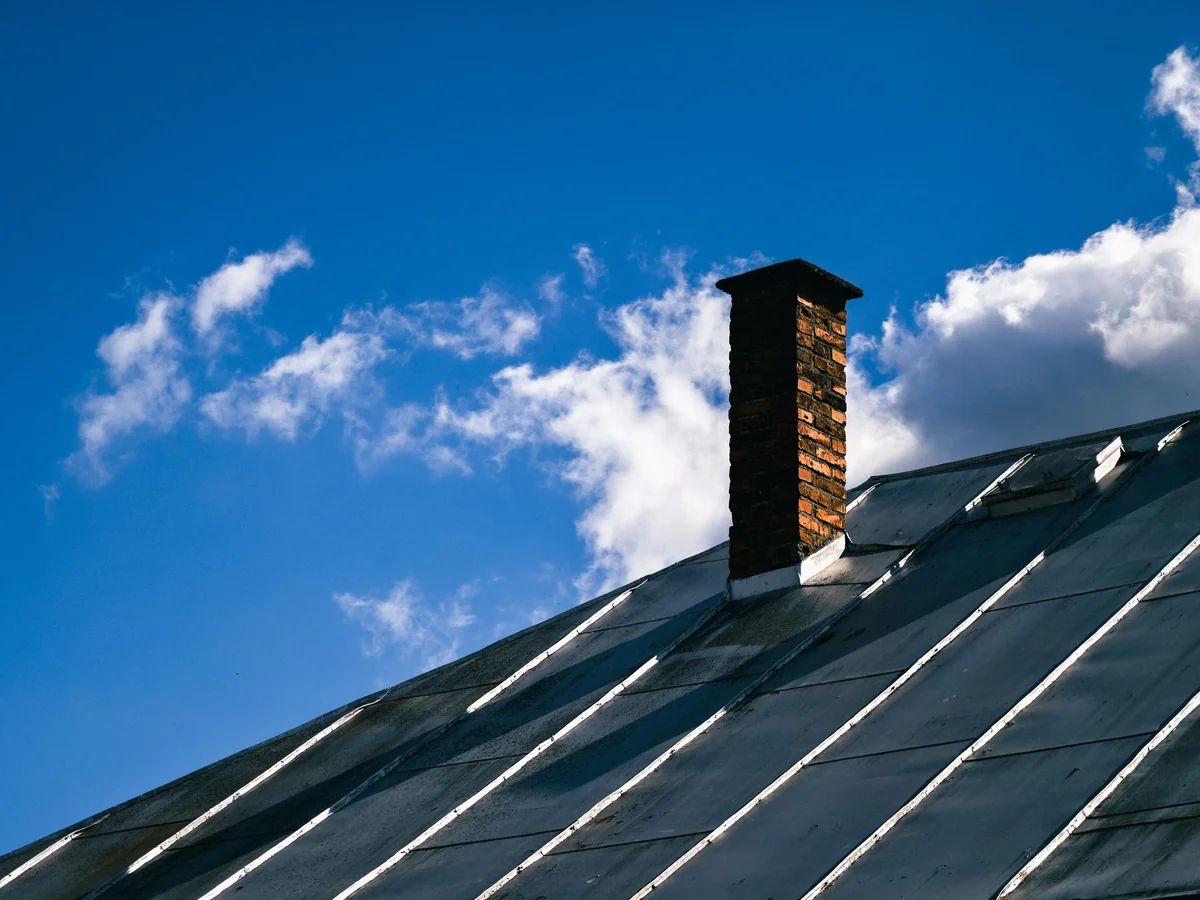 Standing-seam metal gable roof with brick chimney against blue sky