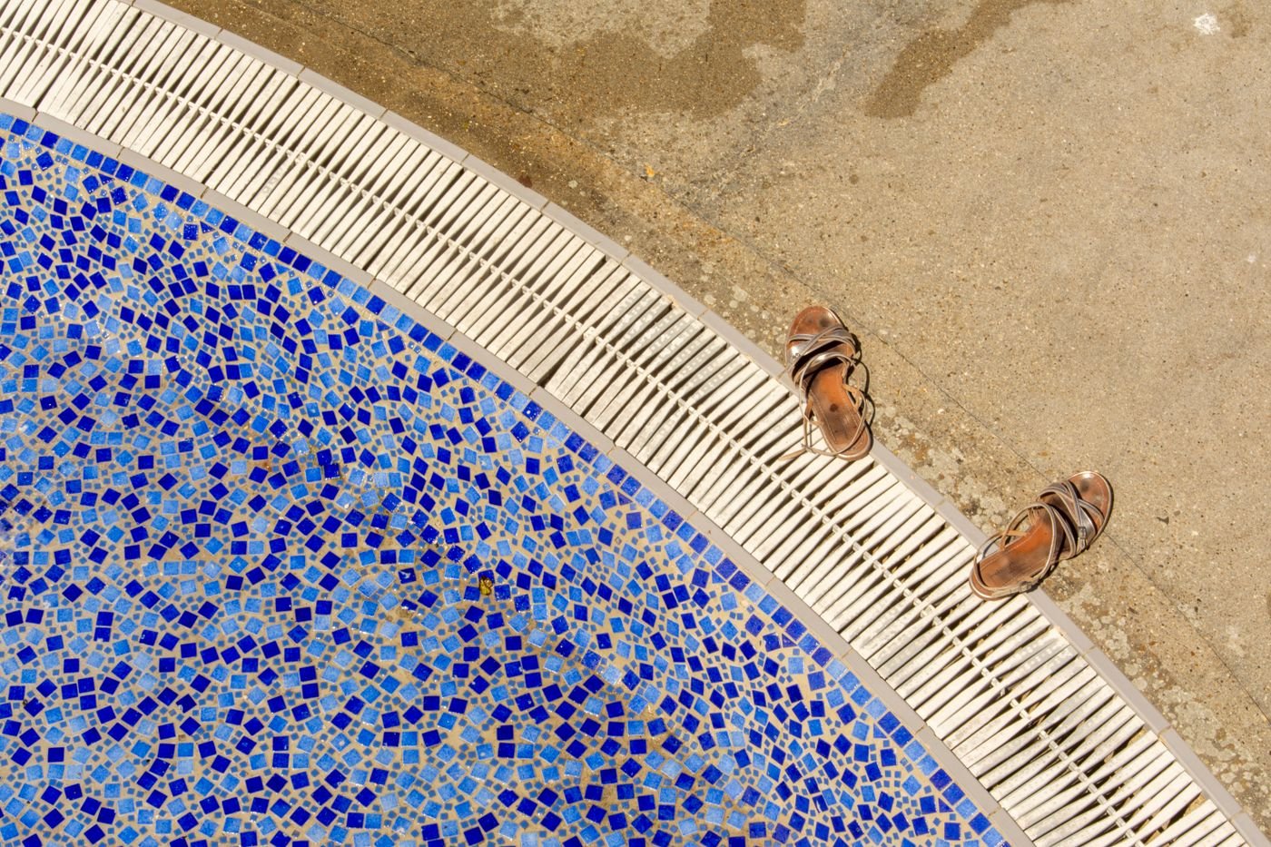 Pool edge ideas: mosaic pool edge with sandals on a concrete pool apron