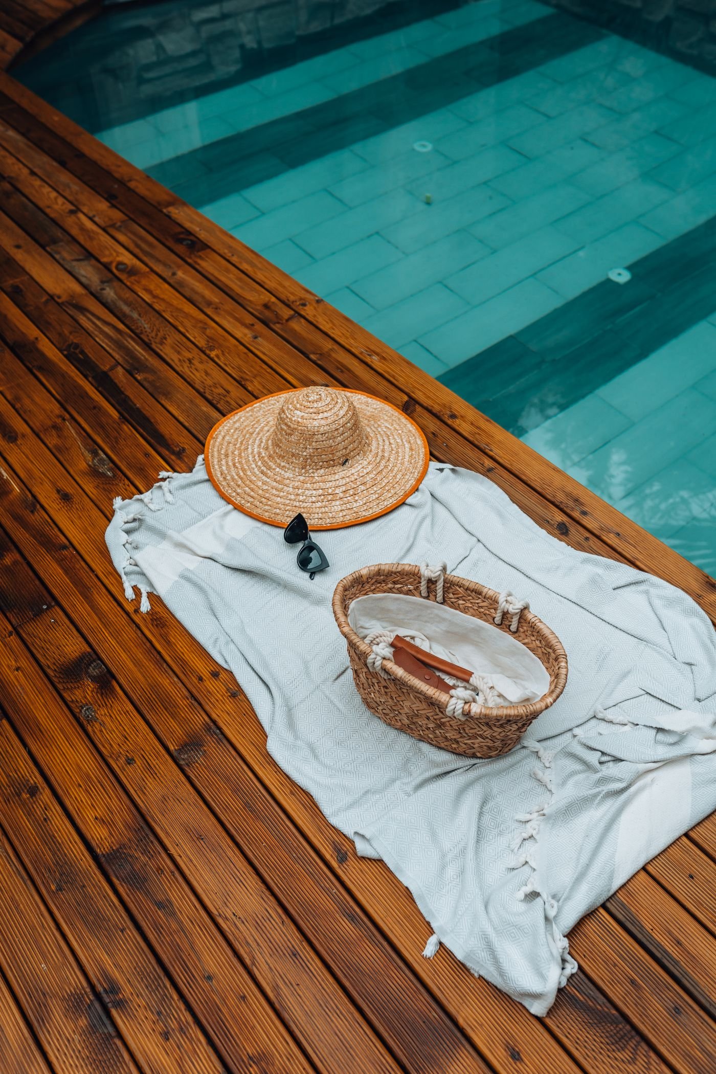 Cheap backyard pool styling: straw hat and basket on wooden planks by the pool